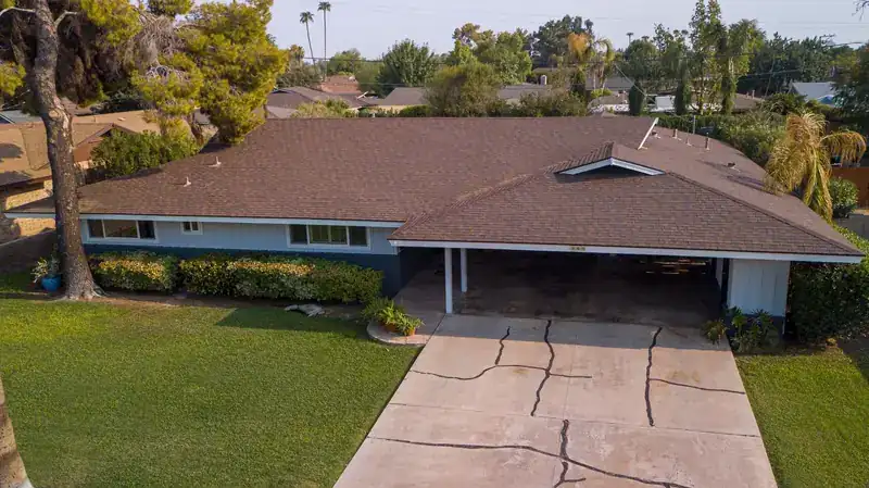 Low-angle aerial view of a single-story house with a brown shingle roof